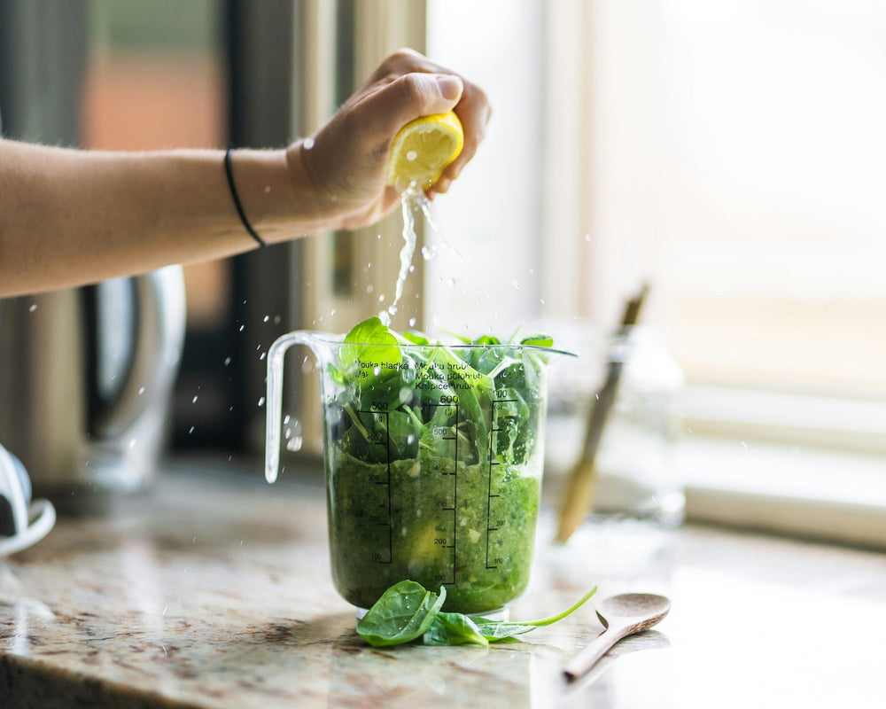 Lemon being squeezed into a blender jug of spinach for a green smoothie